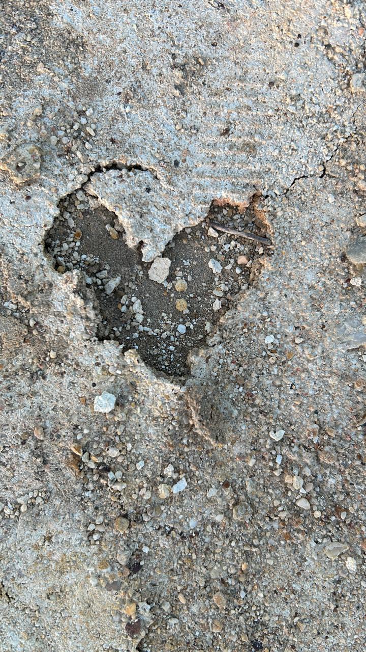 A heart-shaped hollow worn into a sunlit stone surface, revealing deeper earth and small pebbles within